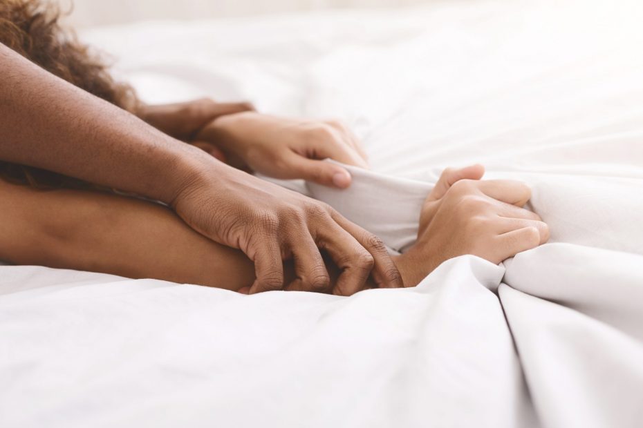 Страсть в постели. Афро-американская пара тянет руки за белые простыни в экстазе, крупный план