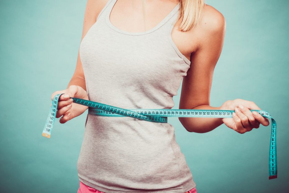 Viktminskning, smal kropp, hälsosam livsstil koncept. Fit fitness tjej mäta sin midja med måttband på blått.